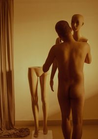 Rear view of shirtless man standing against wall at home