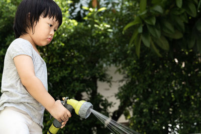 Funny moment of 3 year old asian kid playing water with garden hose in backyard. background concept