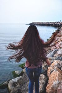 Rear view of woman standing on rock by sea against sky