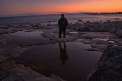 Rear view of man standing at beach during sunset