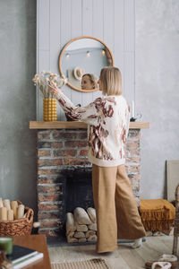 Rear view of woman standing against wall at home