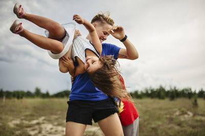 Cheerful siblings playing at park against cloudy sky