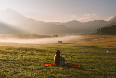 Man sitting on field against mountains