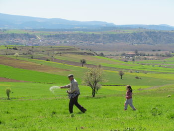 Side view of farmer sprinkling fertilizer by granddaughter on farm