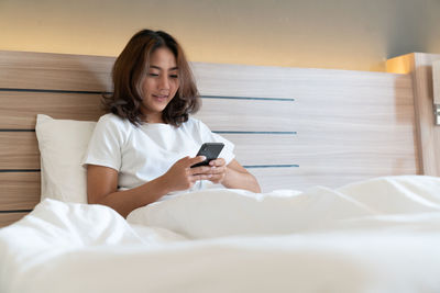 Young woman using phone while sitting on bed at home
