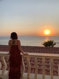 Rear view of woman looking at sea against sunset sky