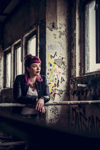 Thoughtful young woman leaning on railing by window in abandoned building