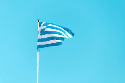 Low angle view of flags against clear blue sky