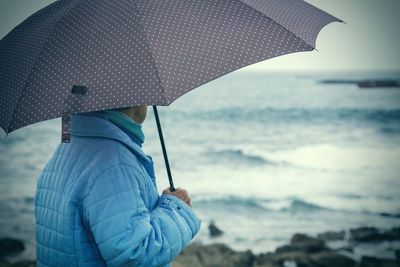 Woman in coat and umbrella in front of the coast