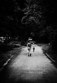 Rear view of people walking on road amidst trees