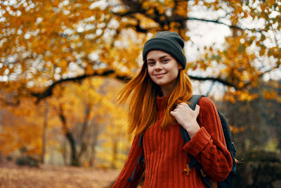 Smiling young woman with autumn leaves against trees