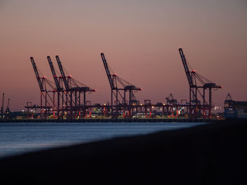 Cranes at commercial dock against sky during sunset