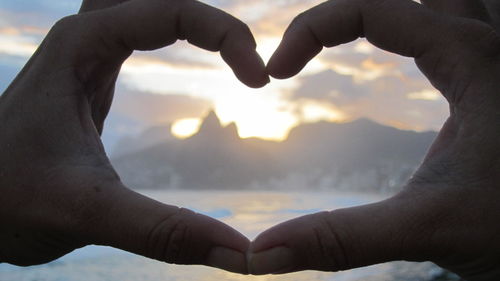 Cropped hands making heart shape against mountain during sunset