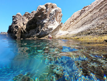 Rock formation in sea against clear blue sky