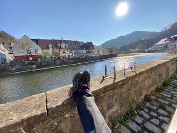 Low section of man on retaining wall by river against sky