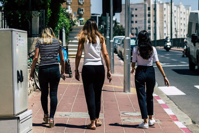Rear view of women walking on footpath in city