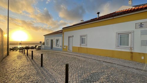 Street by buildings against sky during sunset