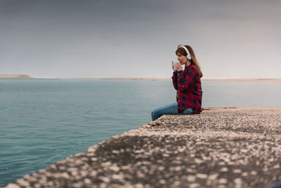 Woman sitting by sea against sky