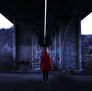 Rear view of woman wearing red hood while standing below bridge