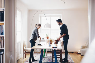 Side view of couple arranging objects on dining table at home
