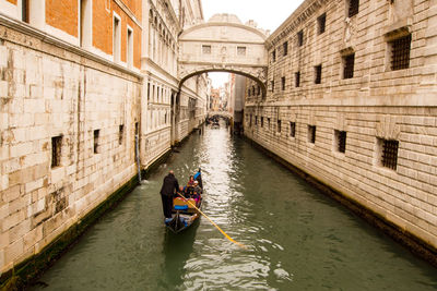 People on boat in canal amidst buildings