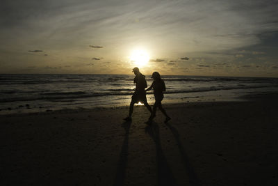 Silhouette friends standing on beach against sky during sunset