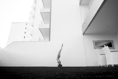 Side view of woman practicing headstand against building
