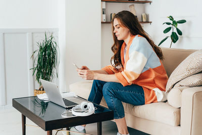 Concentrated young business woman working at home with mobile phone and laptop.