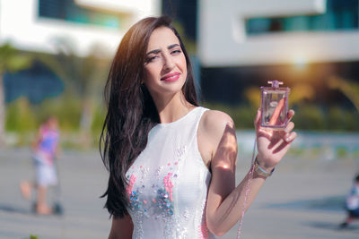 Portrait of smiling woman showing perfume bottle