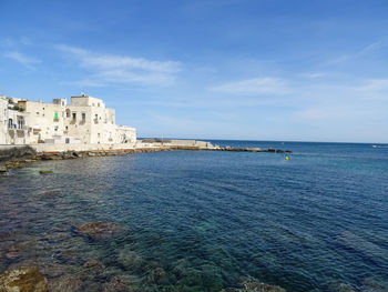 Buildings by sea against blue sky