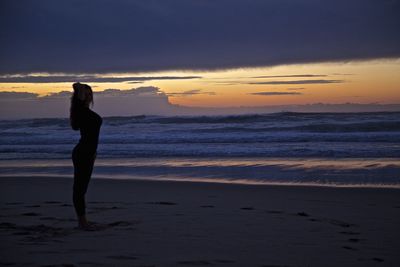 Silhouette woman standing at beach against cloudy sky during sunset