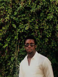 Portrait of young man wearing sunglasses while standing against plants