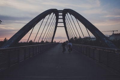 Rear view of friends riding bicycles on bridge during sunset