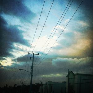 Low angle view of electricity pylon against cloudy sky