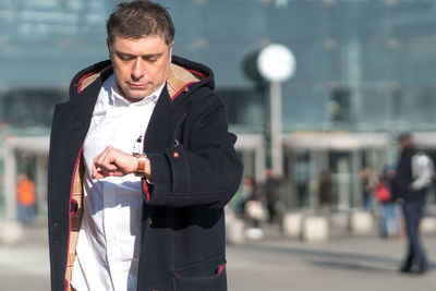 Man checking time while standing against building