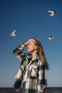 Happy young woman dancing near the sea. seagulls flying on background