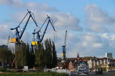 Cranes by buildings against sky in city
