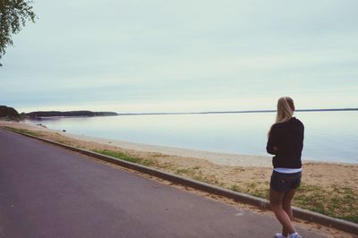 Rear view of woman standing on sea shore against sky