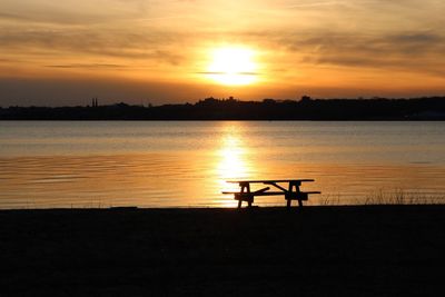 Picnic table at beach against sky during sunset