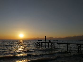 Silhouette people standing on shore against clear sky during sunset