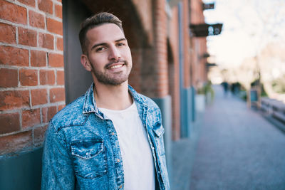Portrait of young man standing against brick wall