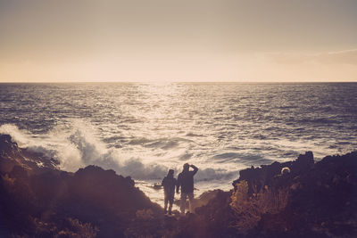 Couple standing on shore at beach against blue sky