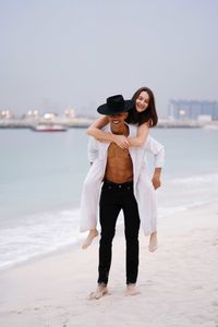 Full length of young couple standing at beach against clear sky