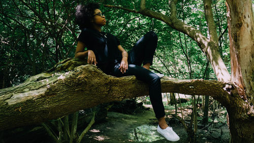 Young woman sitting on tree trunk in forest