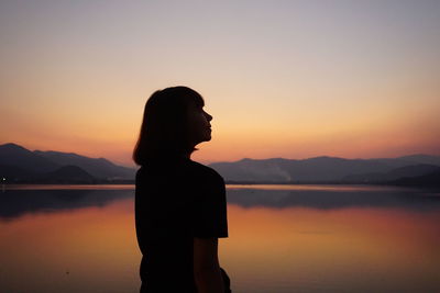 Silhouette woman standing by sea against sky during sunset