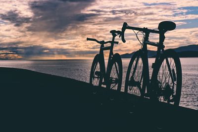 Bicycle on beach against sky during sunset