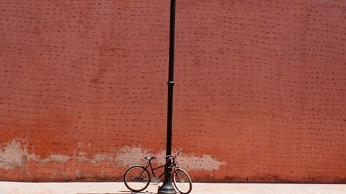 Bicycle parked by pole against brown wall