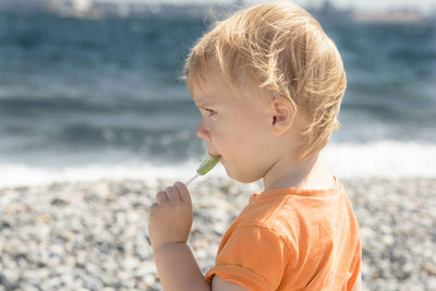 Side view of boy blowing dandelion at beach