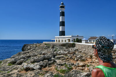 Low angle view of lighthouse by rocks against clear sky