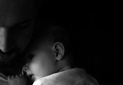 Close-up of man with baby girl against black background